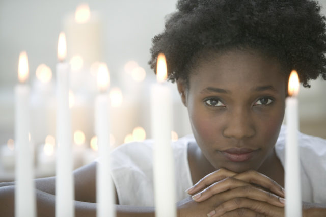 African American woman praying among votive candles, white shirt, Why you should pray when things go wrong