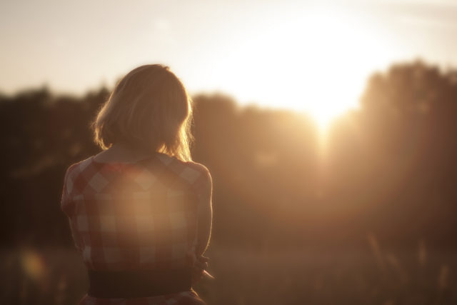 young woman in a plaid shirt watching the sunset from a field, gentleness